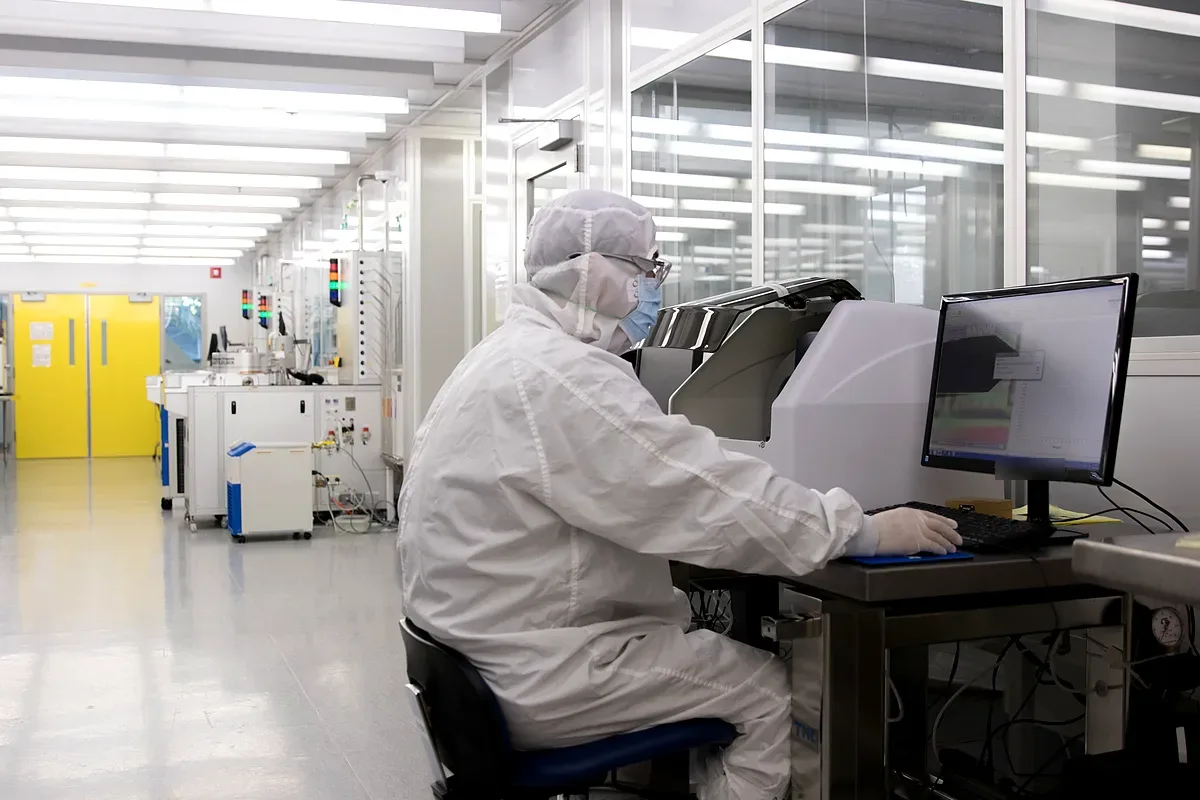 Engineer in full cleanroom suit, mask and gloves at a tool workstation